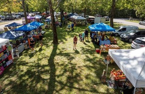 an aerial view of some craft fair vendors, colorful pop up tents amid the trees in the beginning of fall color
