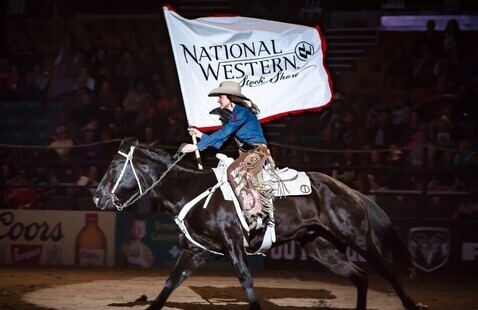 Woman riding horse, carrying "National Western Stock Show" flag