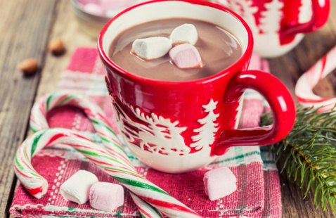 A mug of hot chocolate sitting on a festive table with candy canes and marshmallows