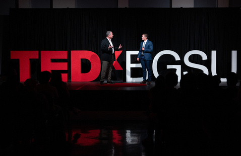 Big letters reading TEDxBGSU in red and white with 2 men speaking in front 