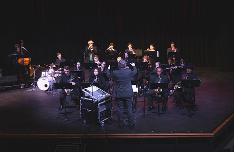 A conductor conducting a jazz band on a stage.