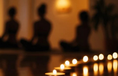 Photo of lit candles in the foreground with the silhouettes of people doing yoga in the background.