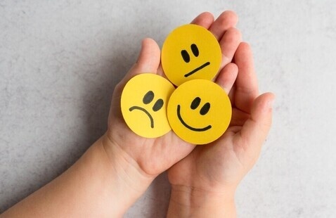 Child's hands holding paper faces with various expressions.