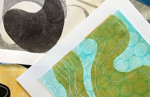 An arrangement of abstract monotype prints layered on a flat surface. The prints showcase organic, flowing shapes and patterns in contrasting colors: one features bold black curves on white, another displays turquoise and green waves with circular textures, and a third uses warm golden tones. Thin white contour lines accentuate the fluidity of the designs, giving a sense of movement and harmony.