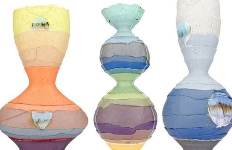 A set of three ceramic vessels with layered, colorful bands creating a stacked, sculptural appearance. Each piece has a unique hourglass-like silhouette and features horizontal layers in pastel tones such as yellow, orange, green, blue, purple, and white. The surfaces are textured with visible seams between layers, and each vessel has an irregular patch of glossy glaze that contrasts with the matte finish of the surrounding clay.