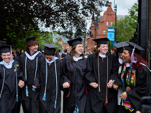 Smiling newly graduated students walk through the Gates, holding hands.