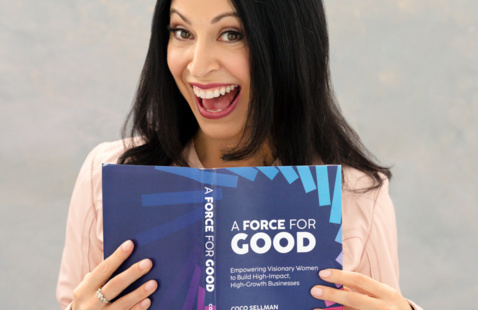 woman with dark hair holds a book with a blue cover.