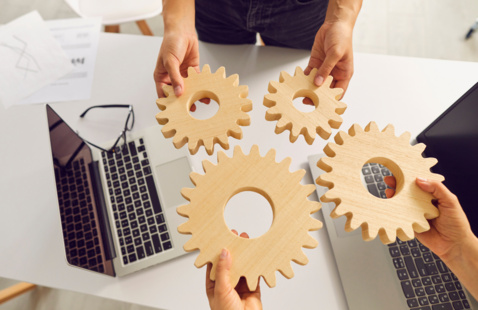 Two sets of hands holding gears over two work laptops