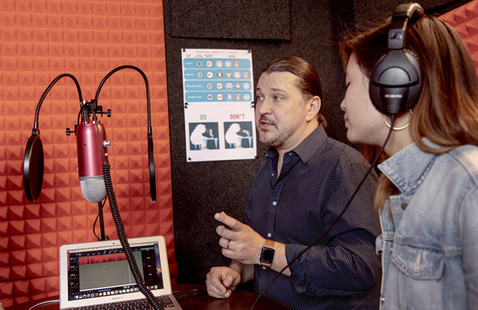 Two women talking at table with computer - bookshelf in background