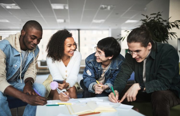 Four people sitting together at a table, writing on papers and discussing.