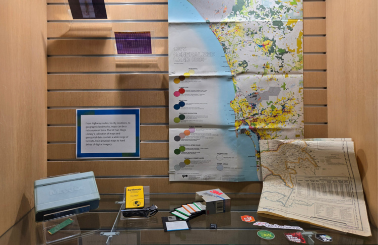 Materials in exhibit case, including maps, disks, stickers, and other didactic information panels.