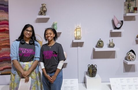Two student guides standing in front of a wall displaying various objects
