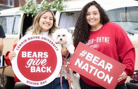 Two LR students and dog pose with Bears Give Back signs during campus event