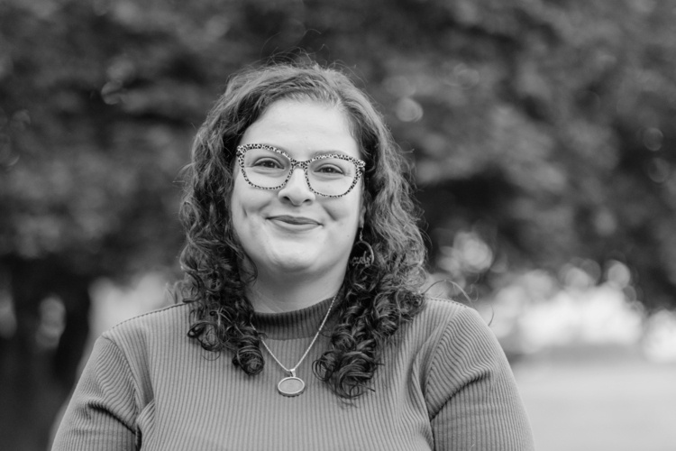 Shomali stands outside and smiles at the camera. 