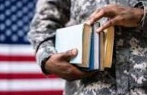 Military student holding books with a U.S. flag in the background