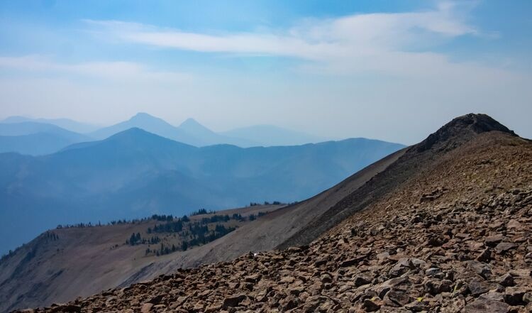 A photo of a rocky mountain range with a blue sky and blue mountains in the background.