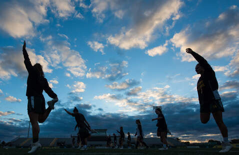 The women's lacrosse team warms up by stretching at sunrise.
