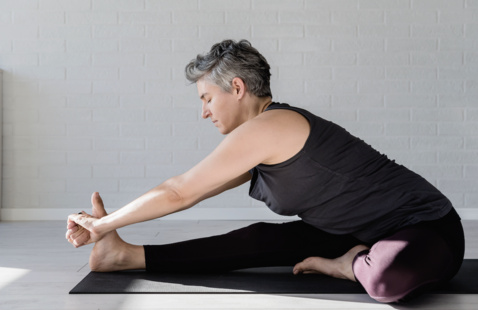Woman leaning forward and stretching, wearing a gray tank top and black leggins