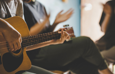 Person playing guitar sitting next to a person clapping