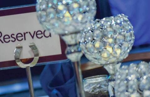 An awards banquet table, decorated with Nevada Silver and Blue colors, ornate crystal glasses, warm lit candles, and seating place signs in silver holders.