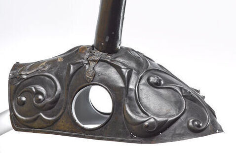 A metal helmet for a horse features two round holes for the horse's ears and two curved horns on top.