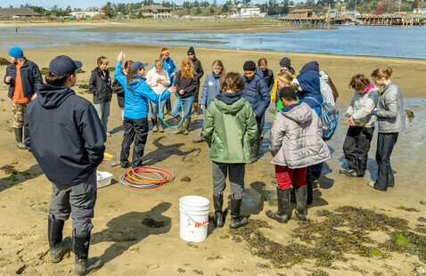 A group of people stand in an estuary with a bucket and hula hoops.