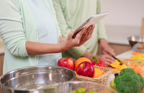 Two adults getting ready to cook, watch and follow the recipe from a tablet