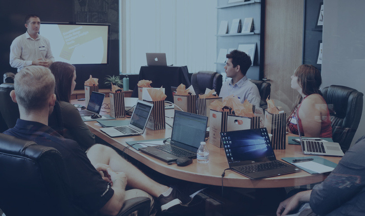 a person leading a small seminar group – standing in front of a group of people seated around a small conference table
