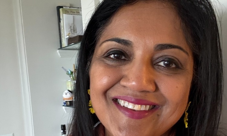A South Asian woman smiling. She is wearing gold earrings. 