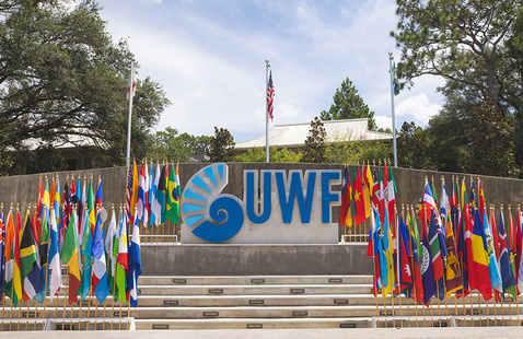 Various country flags on poles displayed on the stairs in front of the UWF campus entrance monument sign.
