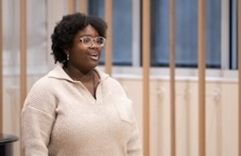 Singer performing at vocal recital wearing cream colored sweater and glasses.