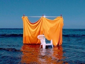 A white plastic lawn chair in front of a yellow curtain sitting in a body of water.