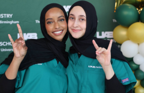 Two dental students in front backdrop and balloons holding up hands for a photo