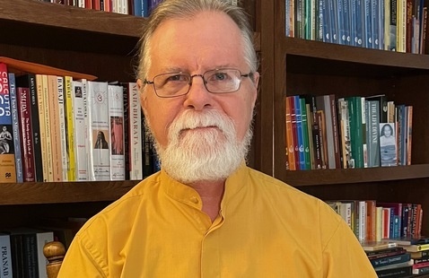 portrait of bearded man in front of a full bookshelf.