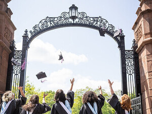 Students throwing their caps in the air in front of the Gates.
