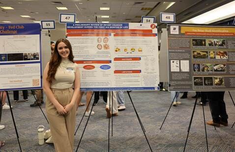 Student standing by their poster at URS 2024
