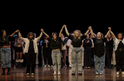 Students on stage raising their hands together and holding hands. 