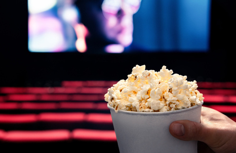 Shutterstock image of someone eating popcorn while watching a movie.