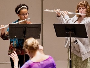 a previous Flute Choir performance. The photo is zoomed in showing two performers, with the conductors head visible in the foreground.