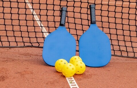 Pickleball racquets and balls sitting up against the net
