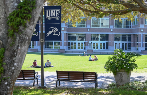 UNF Green with students sitting on grass and UNF sign