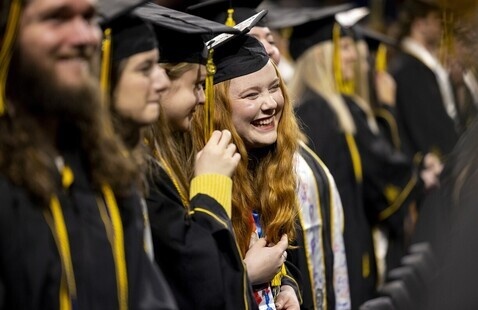 A group of graduates wearing black caps and gowns stand in a line during a commencement ceremony.