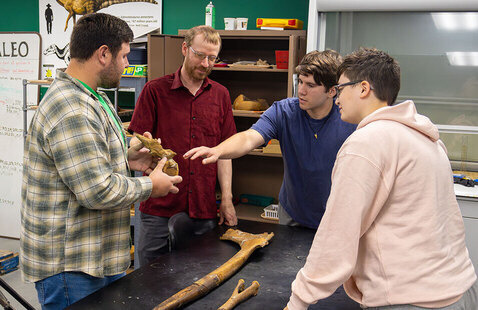 Three students and a paleontologist piece together dinosaur bones in a UND lab.