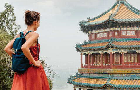 Woman standing on a walkway overlooking intricate, pagoda style building with the sea in the distance. book cover with title