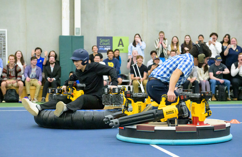 students ride hovercrafts in front of a crowd of students.