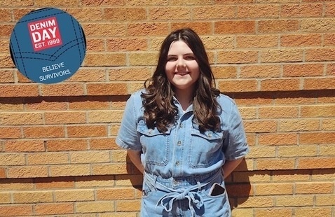 Person wearing a denim jumpsuit up against a brick wall.