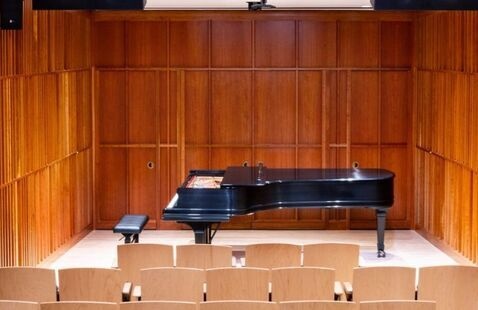 piano in the center of a stage with empty rows of seats in front of it.