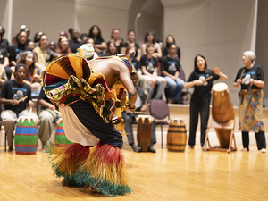 West African Music Ensemble performance. Someone is dancing in the foreground with percussionists in the background.