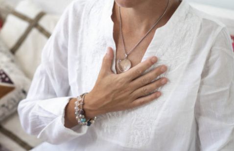 A person in a white embroidered shirt placing their hand over their heart.