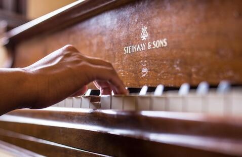 Close up of a hand on a piano keyboard with the brand name in the center "Steinway & Sons"